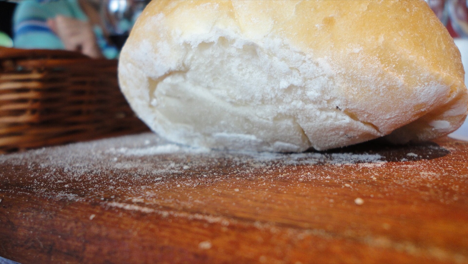Pagnotta di pane artigianale infarinata, appena sfornata su un piano di legno.